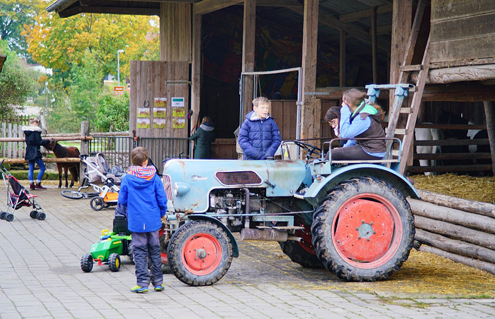 mehrere kinder mit traktor vor pferdestall