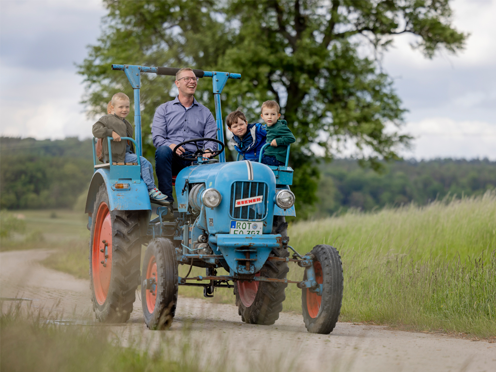 vier Kinder fahren mit Mann auf einem alten Traktor
