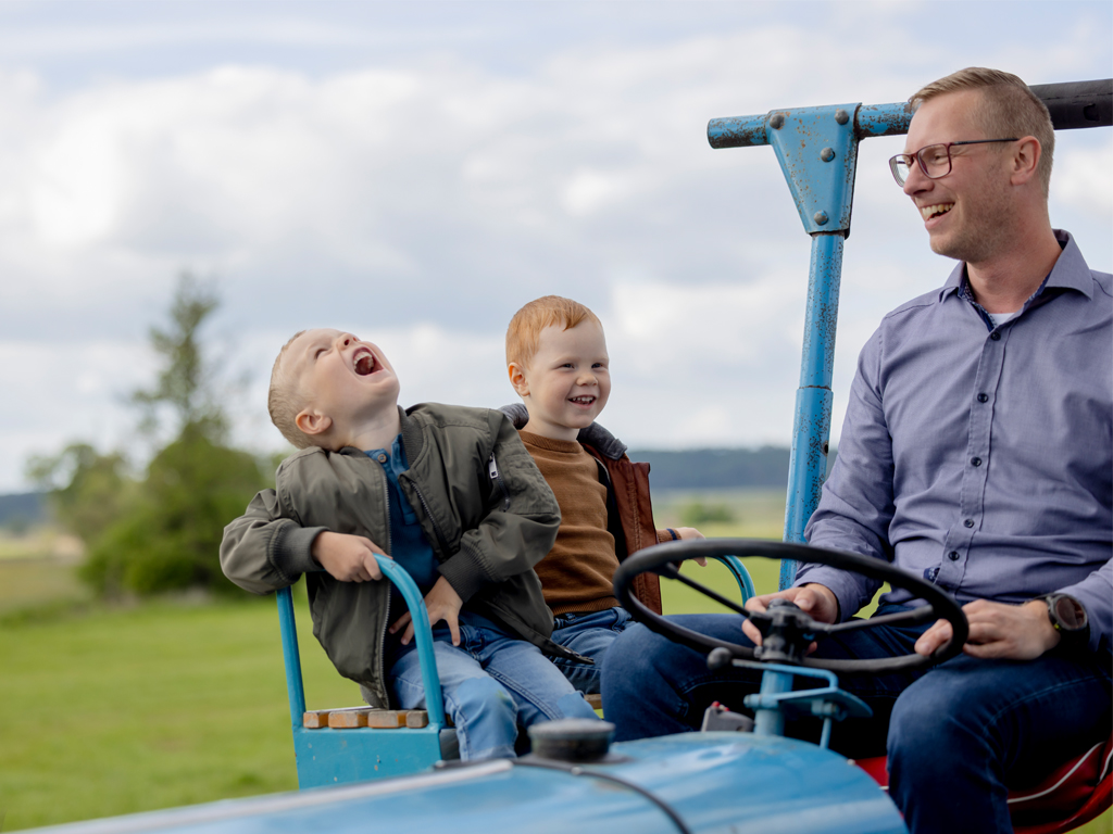 Mann fährt mit 2 Kindern Traktor, alle lachen